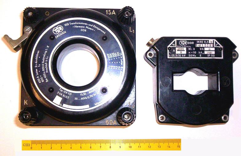 Zwei Stromwandler aus DDR-Produktion nebeneinander vor einem Lineal: links ein runder Ringkernwandler mit Typenaufdruck IKR 0,5, rechts ein kleinerer Wandler mit Typenschild IKRE 0,5 und Aufdruck 300/5 A.