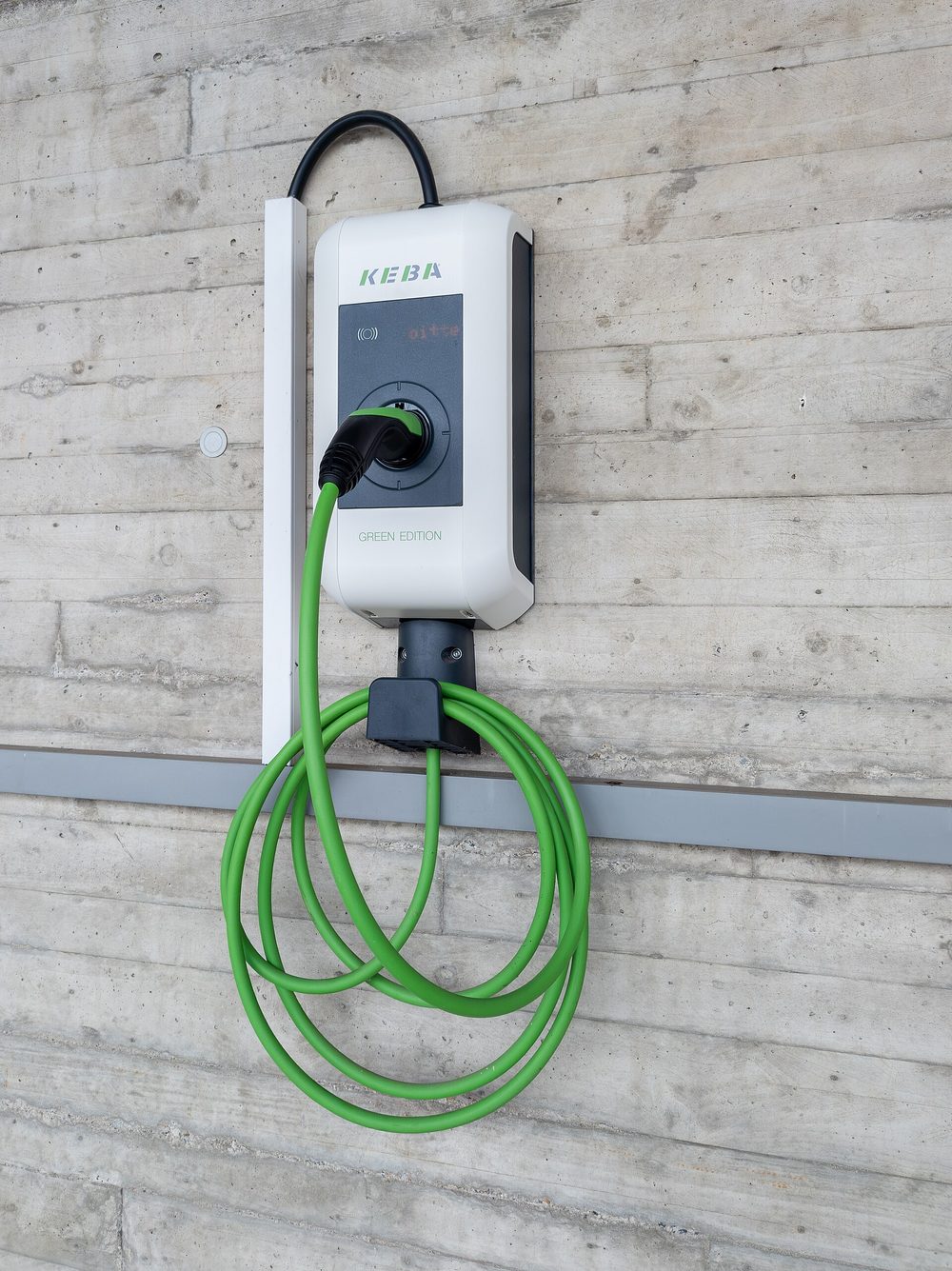 Wallbox Keba KeContact P30 an einer Betonwand: weißes Gehäuse mit dunklem Anzeigefeld, Ladebuchse mit eingestecktem Stecker, grünes Ladekabel auf einer Kabelhalterung