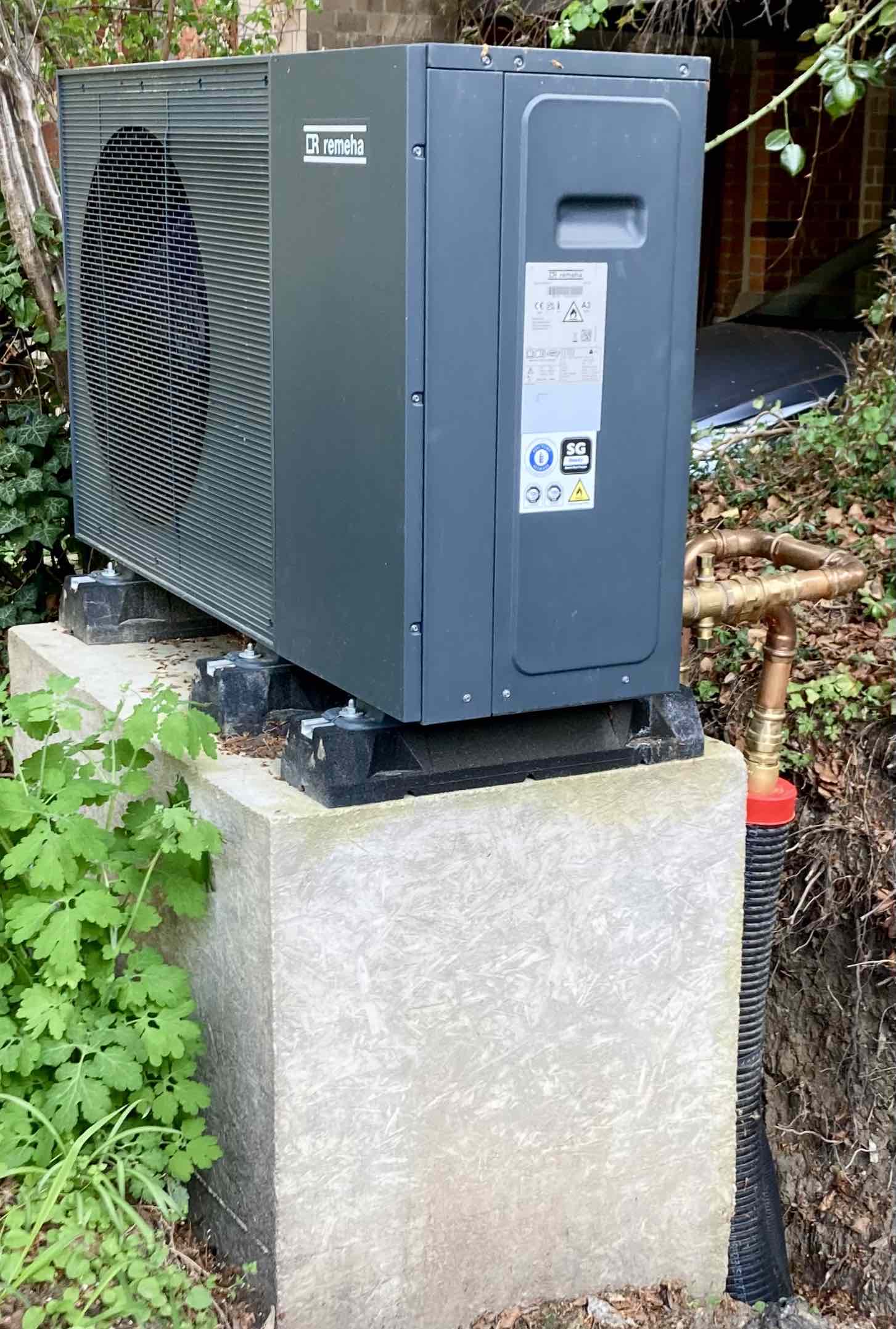 Luft-Wasser-Waermepumpe auf einem Betonsockel neben einem Wohnhaus